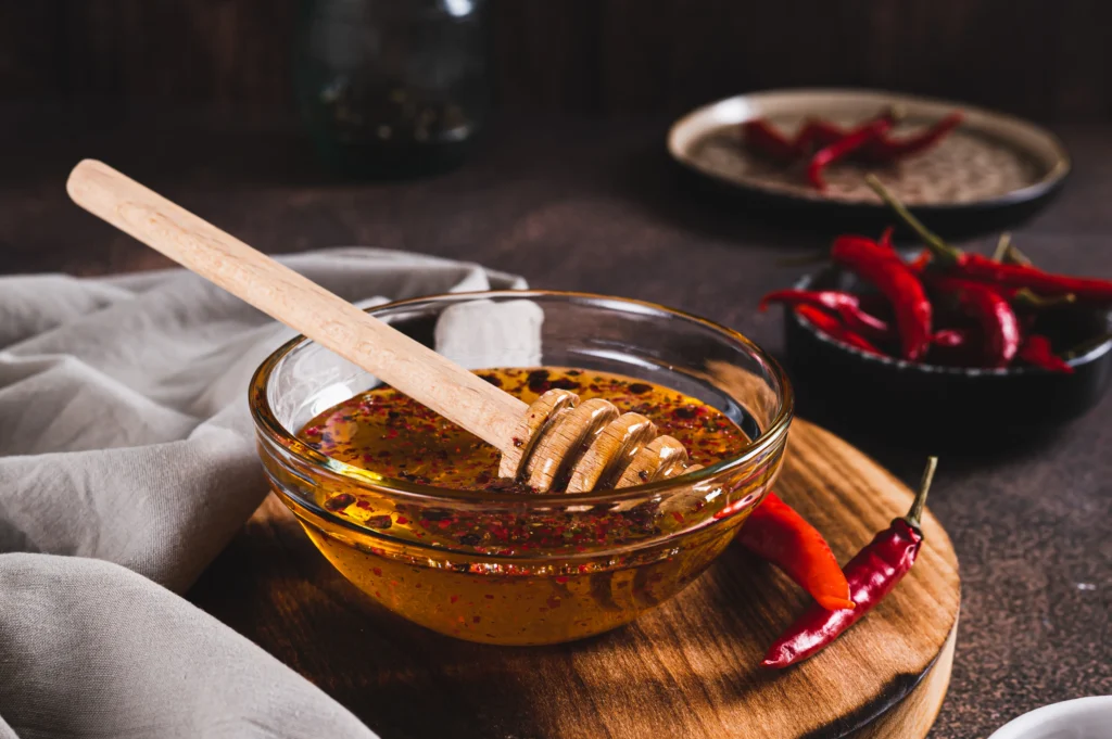 Jar of homemade spicy hot honey being drizzled over crispy fried chicken on a wooden table