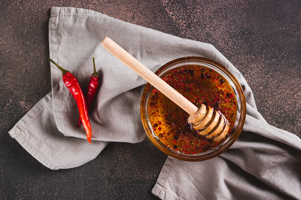 Jar of homemade spicy hot honey being drizzled over crispy fried chicken on a wooden table
