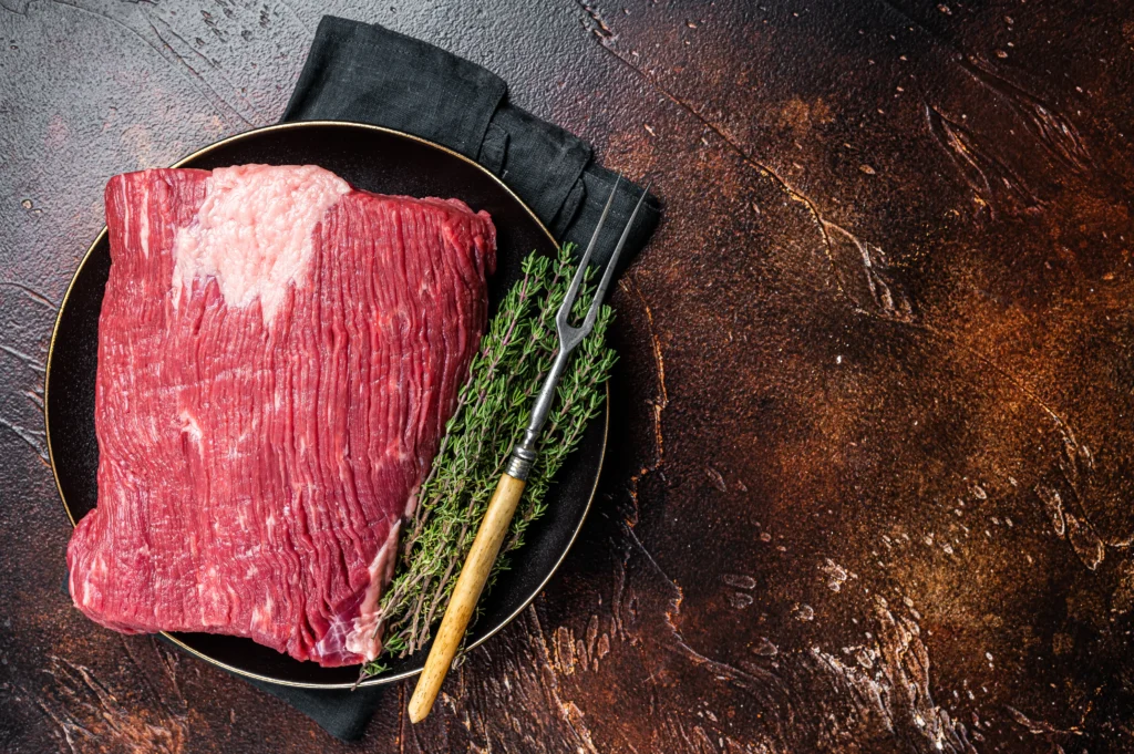 Sliced tender flank steak served on a cutting board with herbs and juices