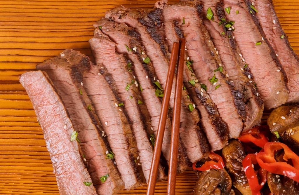 Sliced tender flank steak served on a cutting board with herbs and juices