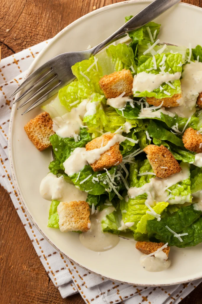 Creamy homemade Caesar dressing in a bowl with fresh salad ingredients on a wooden table