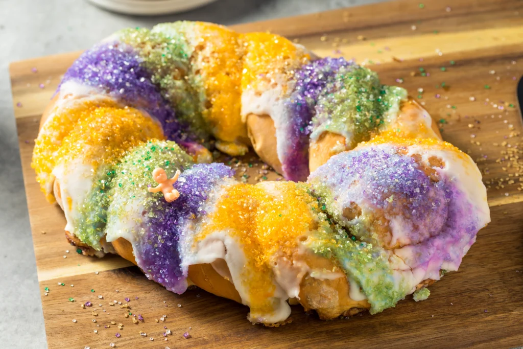 King Cake Recipe
Homemade King Cake decorated with purple, green, and gold sugar icing, sliced to reveal soft cinnamon filling inside on a festive table