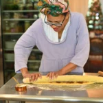 Homemade King Cake decorated with purple, green, and gold sugar icing, sliced to reveal soft cinnamon filling inside on a festive table
