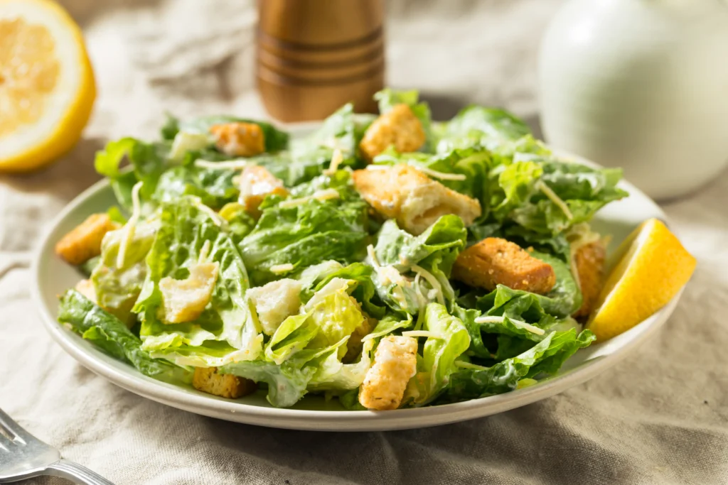 Creamy homemade Caesar dressing in a bowl with fresh salad ingredients on a wooden table