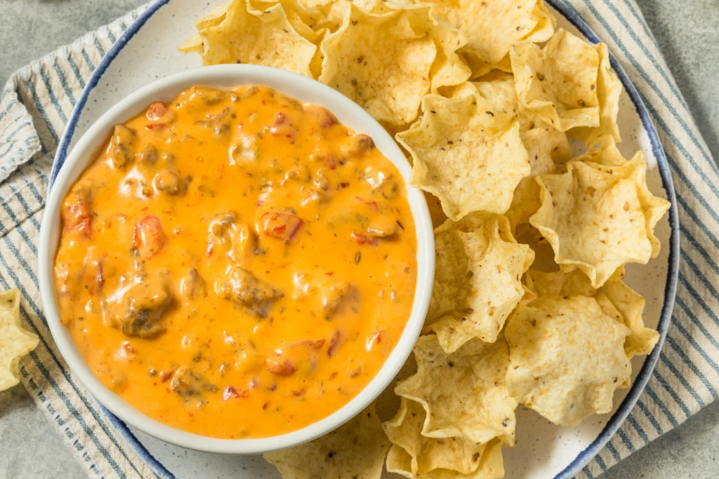 A bowl of creamy Rotel dip made with melted cheese, ground beef, and tomatoes with chilies, served with tortilla chips for game day