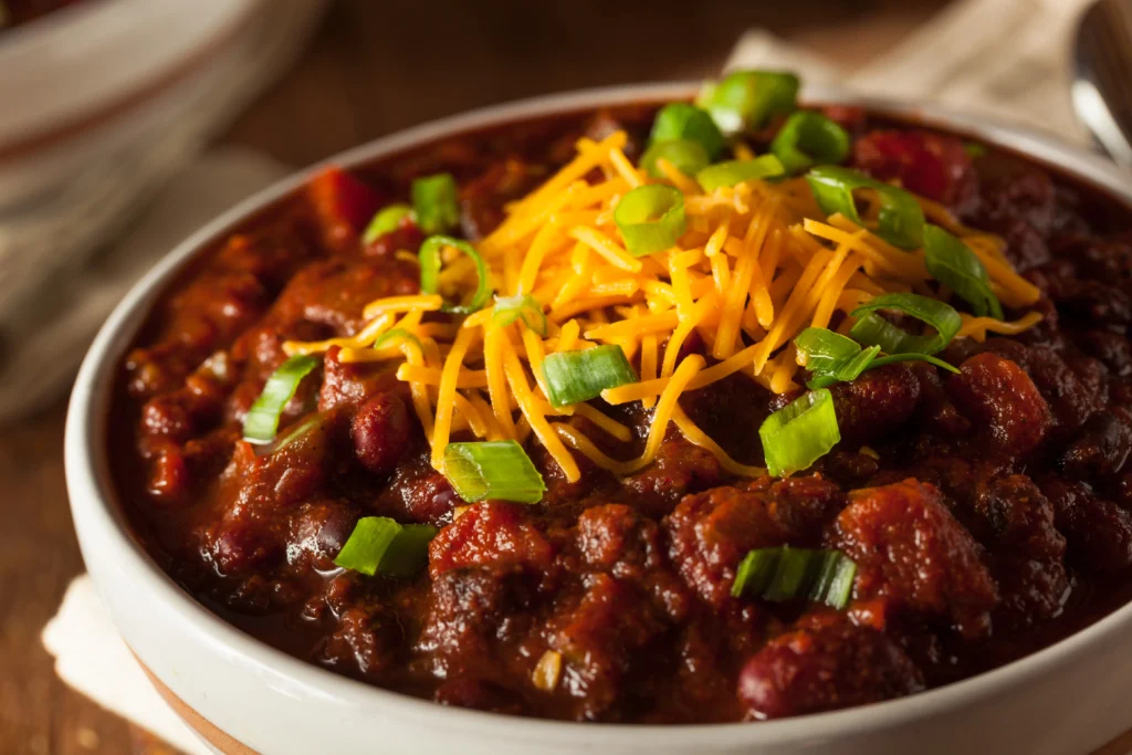 Hearty homemade crockpot chili with beans, peppers, and melted cheese served with cornbread