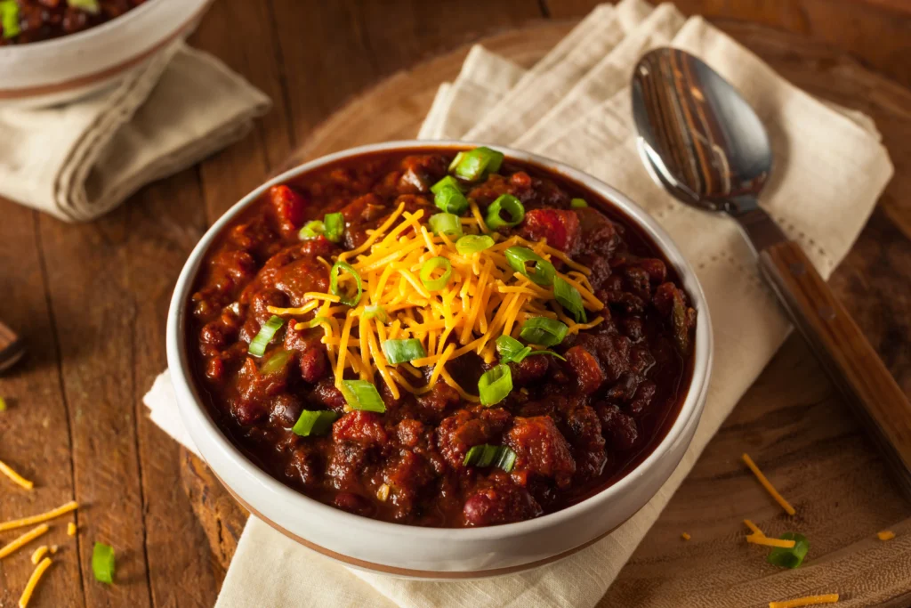 Hearty homemade crockpot chili with beans, peppers, and melted cheese served with cornbread
