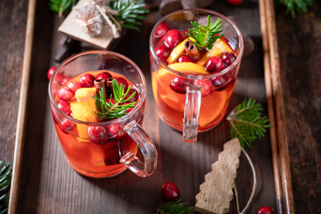 Colorful holiday rum punch cocktail with citrus slices, cranberries, and ice in a festive glass