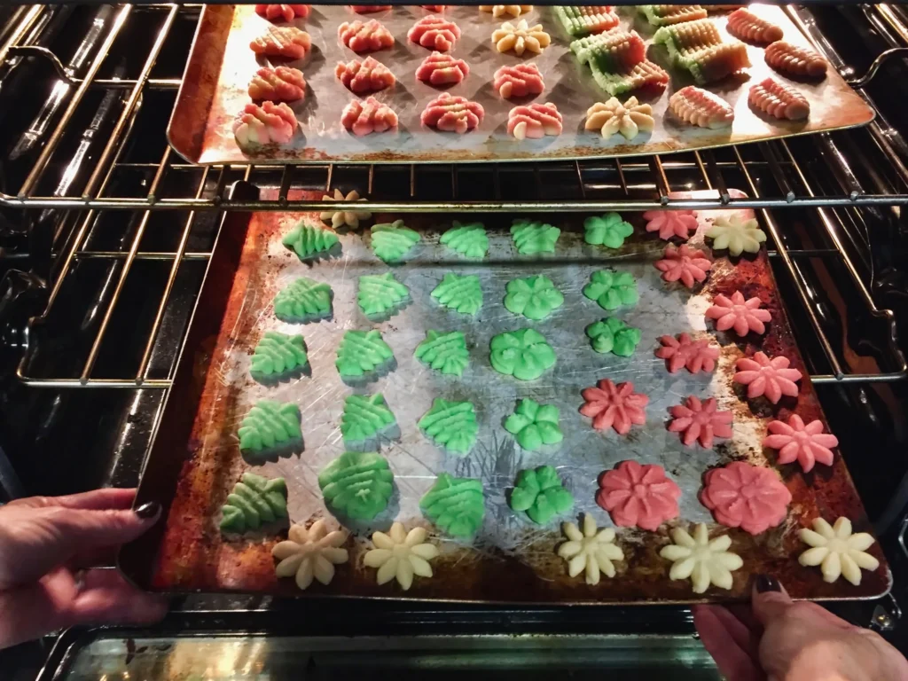 Buttery homemade spritz cookies in festive shapes on a baking tray, freshly baked and golden edges