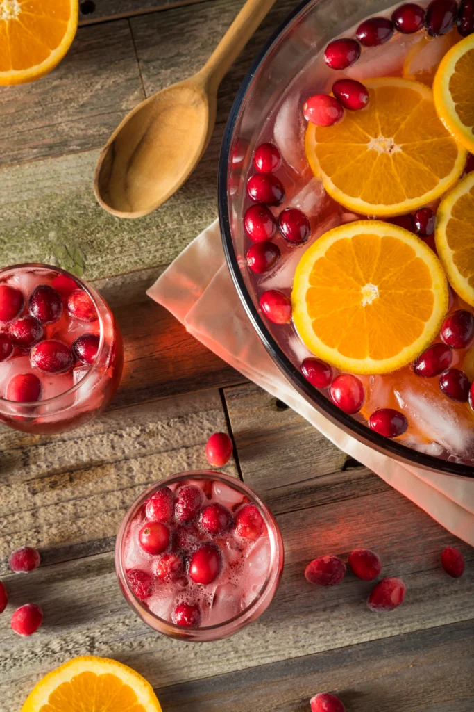 Colorful holiday rum punch cocktail with citrus slices, cranberries, and ice in a festive glass