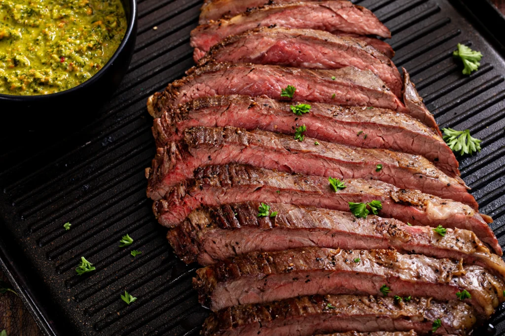 Sliced tender flank steak served on a cutting board with herbs and juices