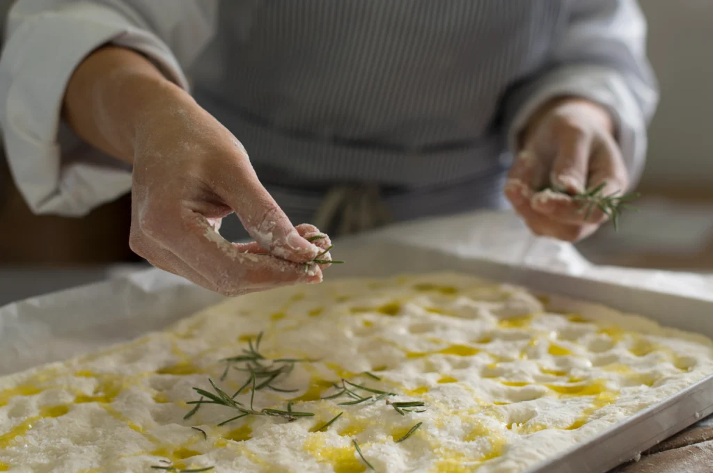 Freshly baked fluffy sourdough focaccia with airy texture, golden crispy crust, olive oil drizzle, and rosemary topping on a rustic wooden table.