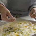 Freshly baked fluffy sourdough focaccia with airy texture, golden crispy crust, olive oil drizzle, and rosemary topping on a rustic wooden table.