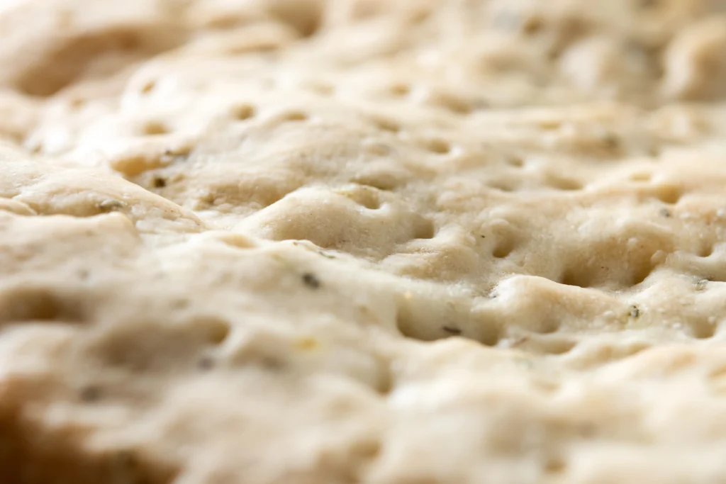 Freshly baked fluffy sourdough focaccia with airy texture, golden crispy crust, olive oil drizzle, and rosemary topping on a rustic wooden table.