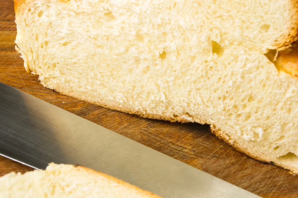 Freshly baked fluffy white sandwich bread sliced on a wooden board, showing a soft and airy texture.