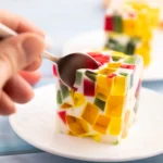 Colorful fruity gelatin dessert topped with fresh strawberries, kiwi, blueberries, and whipped cream in a glass serving dish.