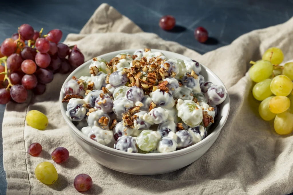 Creamy homemade grape salad with red and green grapes, topped with brown sugar and chopped pecans in a bowl