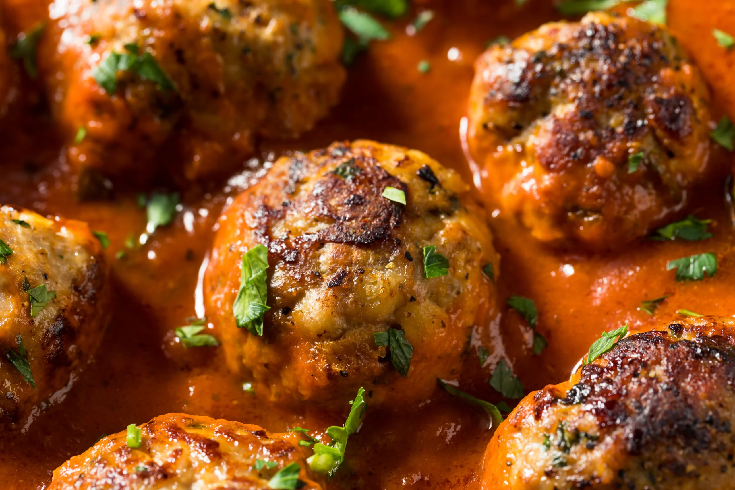 Turkey meatballs simmering in rich tomato sauce in a skillet, served with fresh herbs on top.