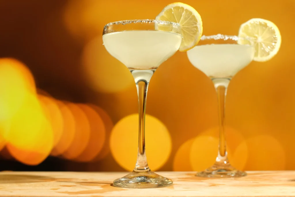 A chilled lemon drop martini served in a sugar-rimmed cocktail glass with fresh lemon slices and a bright yellow cocktail on a modern bar counter.