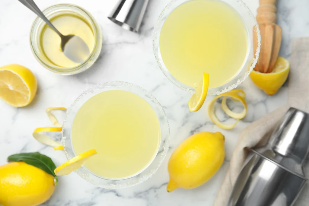 A chilled lemon drop martini served in a sugar-rimmed cocktail glass with fresh lemon slices and a bright yellow cocktail on a modern bar counter.