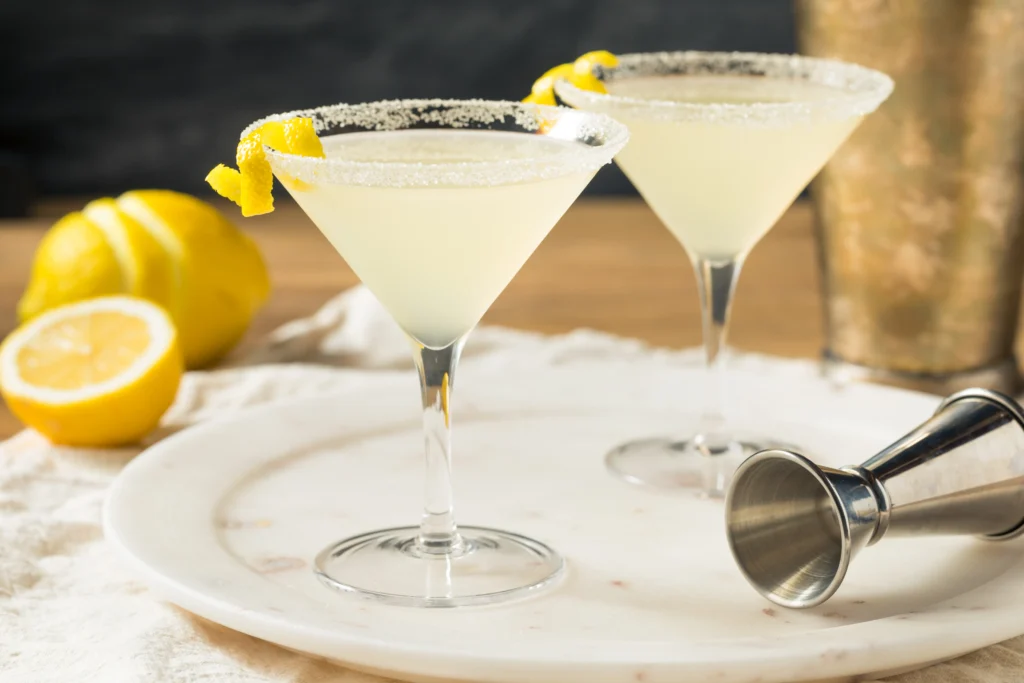 A chilled lemon drop martini served in a sugar-rimmed cocktail glass with fresh lemon slices and a bright yellow cocktail on a modern bar counter.