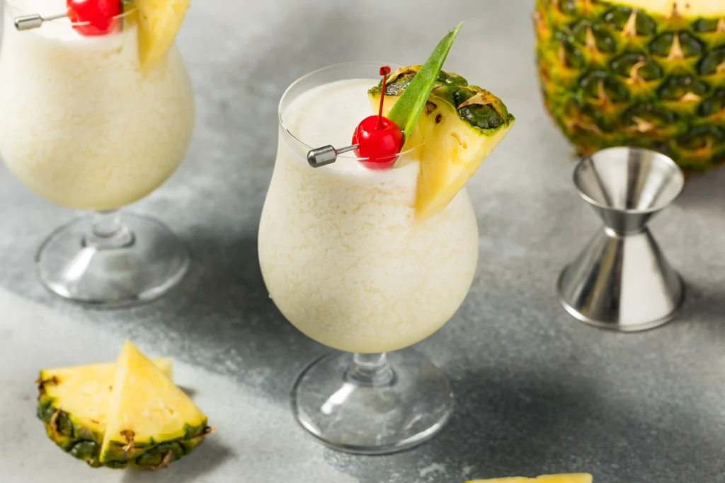 Creamy tropical pina colada cocktail served in a chilled glass with pineapple slices, coconut flakes, and cherries on a summer beach-themed table