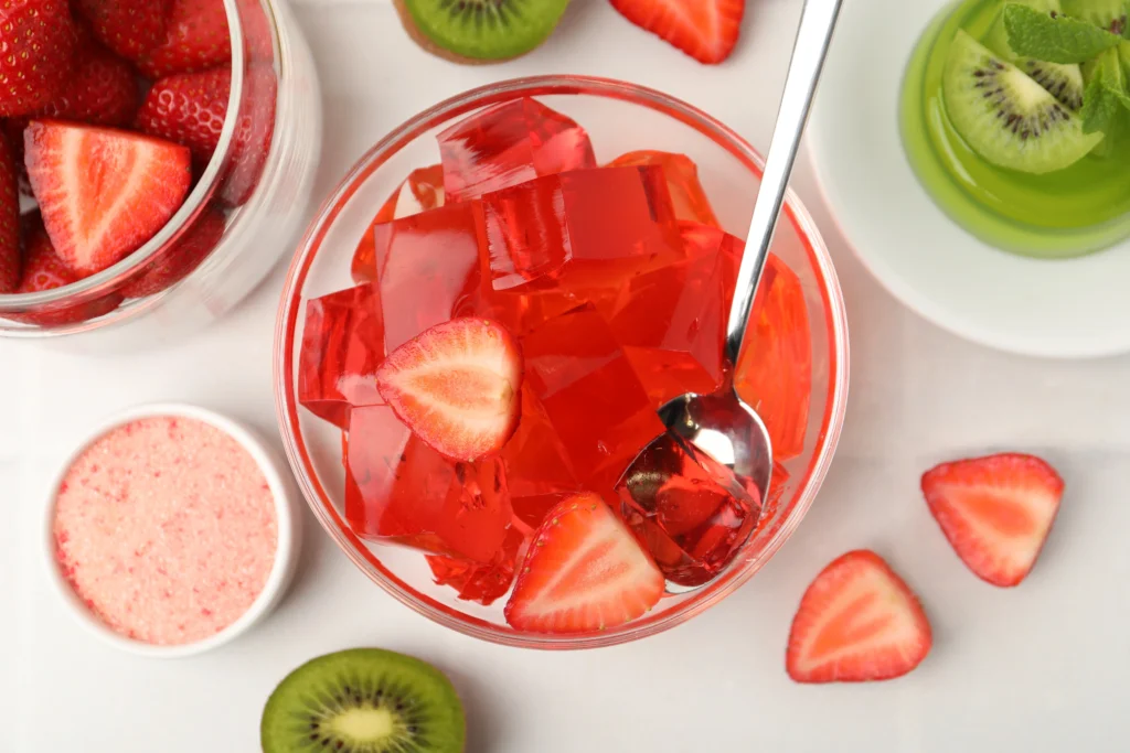 Colorful fruity gelatin dessert topped with fresh strawberries, kiwi, blueberries, and whipped cream in a glass serving dish.