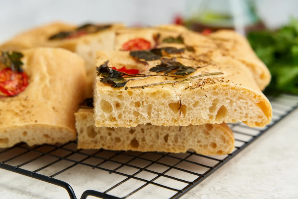Freshly baked fluffy sourdough focaccia with airy texture, golden crispy crust, olive oil drizzle, and rosemary topping on a rustic wooden table.