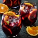 A glass of traditional Spanish sangria with fresh fruit slices including oranges, lemons, and berries served in a pitcher