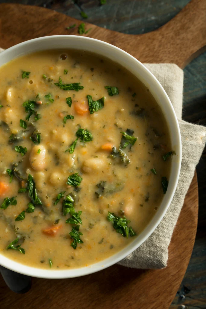 A rustic bowl of Tuscan white bean soup with cannellini beans, kale, carrots, and herbs served warm on a wooden table