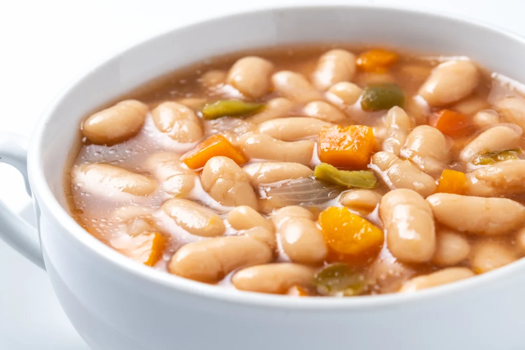 A rustic bowl of Tuscan white bean soup with cannellini beans, kale, carrots, and herbs served warm on a wooden table