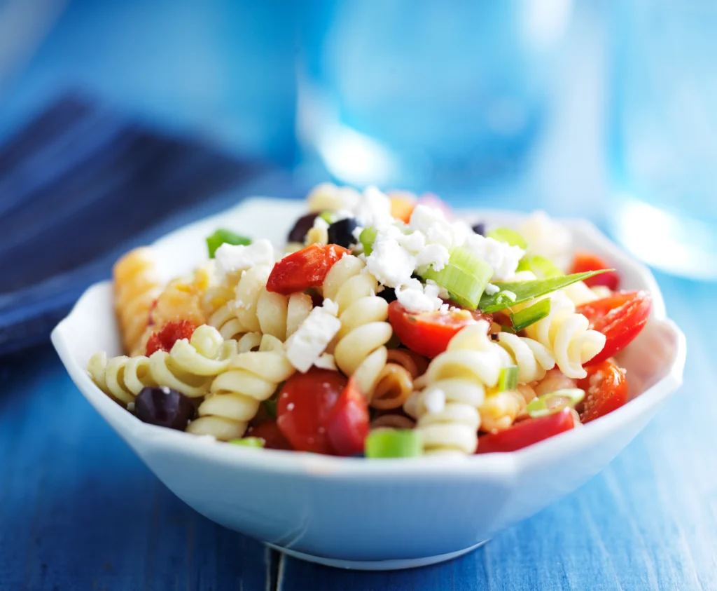 Fresh Tomato & Feta Pasta Salad made with rotini pasta, cherry tomatoes, crumbled feta cheese, cucumber, basil, and a lemon olive oil dressing in a serving bowl.