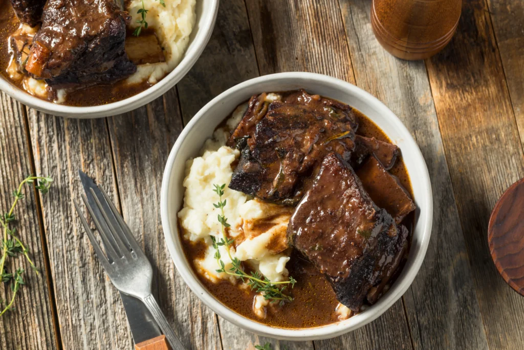 Fall-Off-The-Bone Braised Short Ribs served with rich sauce and vegetables on a rustic plate