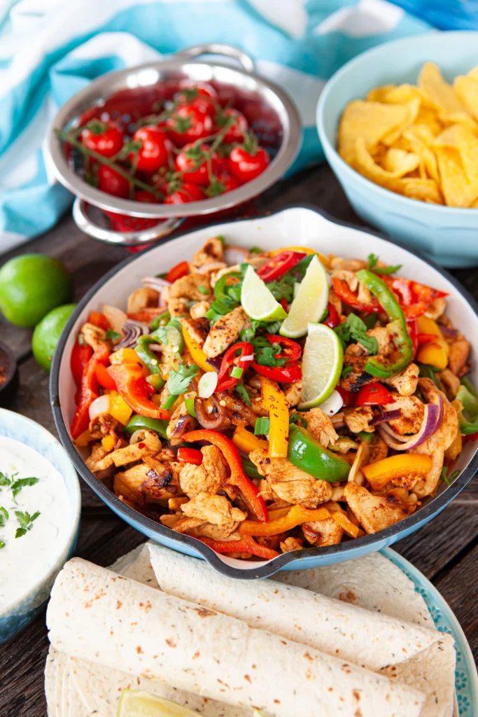 Sheet pan chicken fajitas with seasoned grilled chicken strips, colorful bell peppers, and onions roasted to perfection, served with warm tortillas and fresh lime wedges.
