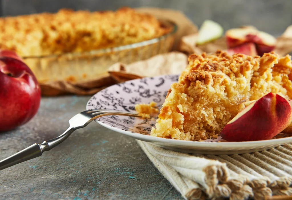 Fresh peach cobbler baked to golden perfection in a rustic dish, featuring juicy sliced peaches beneath a buttery, crisp topping, served warm with a scoop of vanilla ice cream on a sunny summer day.