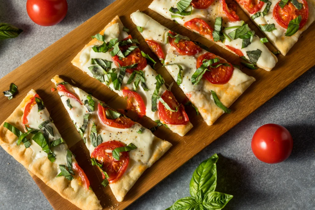 Freshly baked cottage cheese flatbread pizza topped with melted mozzarella, cherry tomatoes, basil leaves, and herbs, served on a wooden board for a healthy high-protein meal.