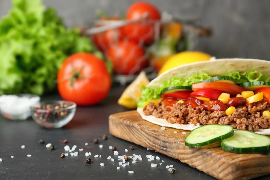 A close-up of restaurant-style smash burger tacos filled with crispy smashed beef patties, melted cheese, fresh lettuce, pickles, diced onions, and creamy burger sauce on toasted tortillas.