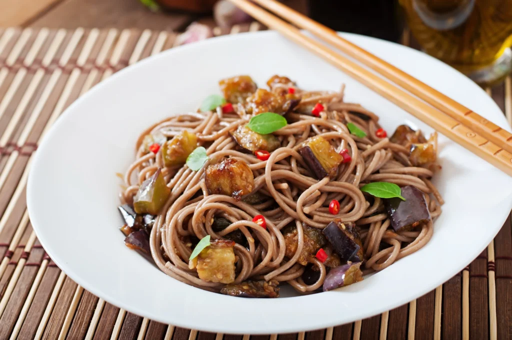 Bowl of cold soba noodle salad with fresh vegetables, edamame, and sesame dressing, served as a light and refreshing summer lunch.