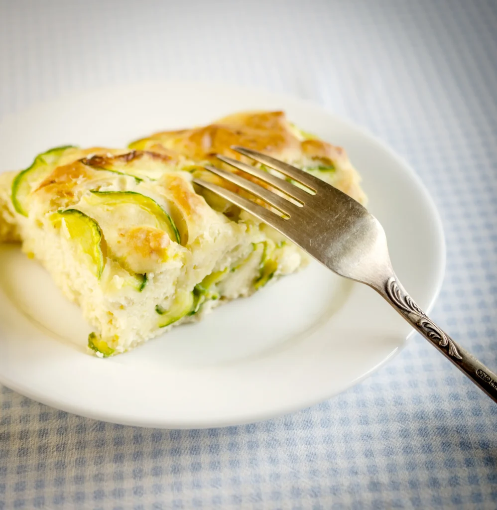 Golden-brown Garden Crustless Zucchini Pie Recipe baked with fresh zucchini, herbs, onions, and melted cheese, sliced and served on a white plate.