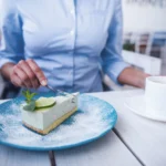 Slice of creamy lime icebox pie topped with whipped cream and fresh lime zest on a graham cracker crust, served on a white dessert plate.