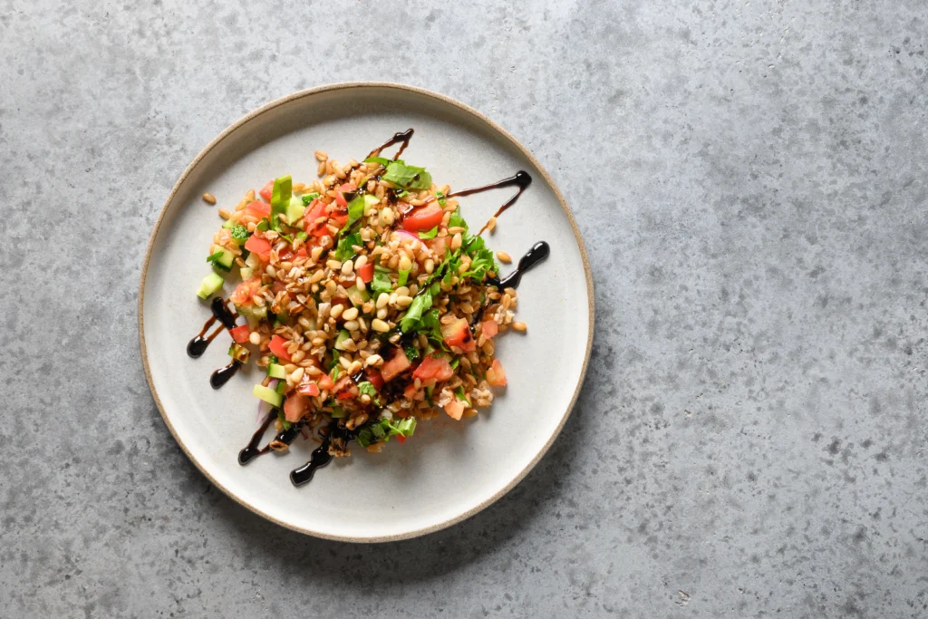 Bowl of viral crispy rice salad topped with fresh vegetables, herbs, and a creamy spicy tahini dressing, served on a wooden table.