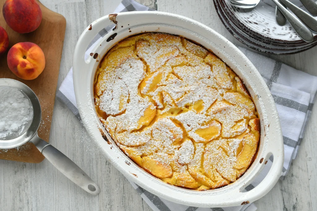 Fresh peach spoon cake served warm in a rustic baking dish, topped with juicy sliced peaches and a golden buttery cake layer, perfect for a comforting summer dessert.