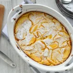 Fresh peach spoon cake served warm in a rustic baking dish, topped with juicy sliced peaches and a golden buttery cake layer, perfect for a comforting summer dessert.