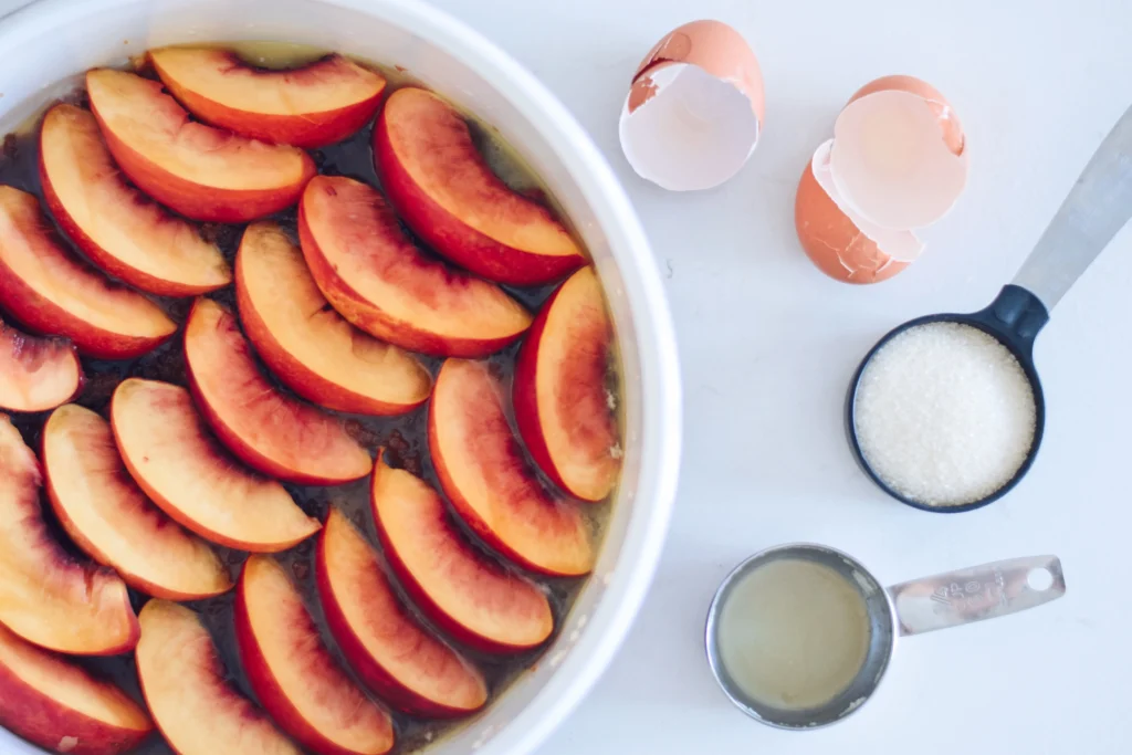 Fresh peach spoon cake served warm in a rustic baking dish, topped with juicy sliced peaches and a golden buttery cake layer, perfect for a comforting summer dessert.