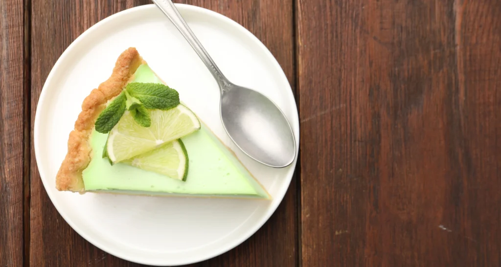 Slice of creamy lime icebox pie topped with whipped cream and fresh lime zest on a graham cracker crust, served on a white dessert plate.