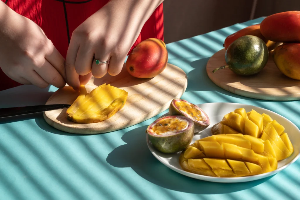 A traditional serving of sweet mango sticky rice topped with creamy coconut sauce, featuring ripe golden mango slices arranged beside glutinous rice and garnished with toasted sesame seeds on a rustic plate.