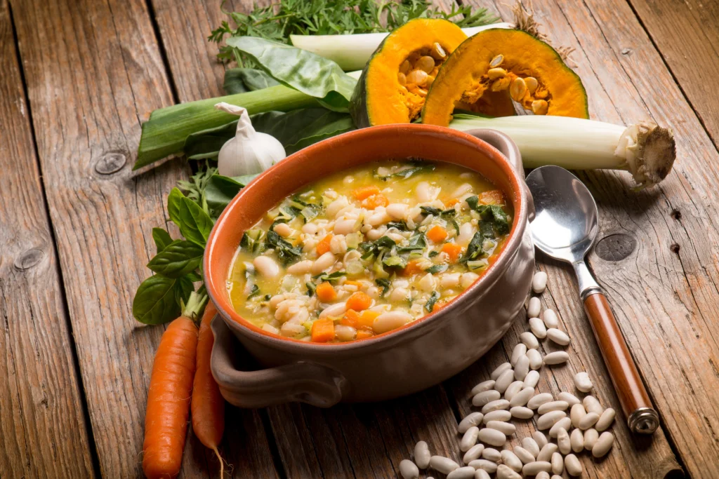 A rustic bowl of Tuscan white bean soup with cannellini beans, kale, carrots, and herbs served warm on a wooden table
