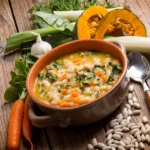 A rustic bowl of Tuscan white bean soup with cannellini beans, kale, carrots, and herbs served warm on a wooden table