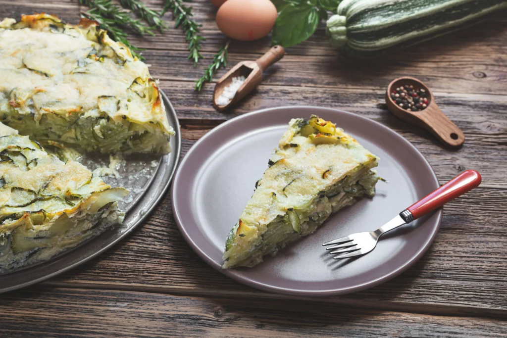 Golden-brown Garden Crustless Zucchini Pie Recipe baked with fresh zucchini, herbs, onions, and melted cheese, sliced and served on a white plate.