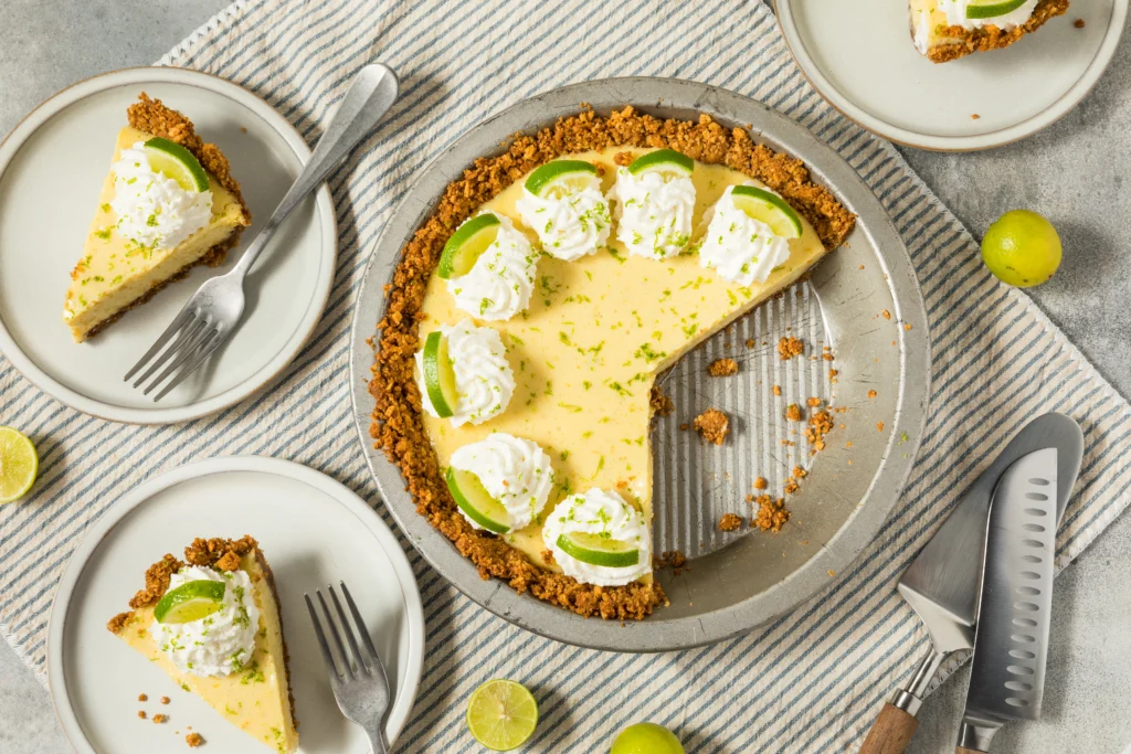 Slice of creamy lime icebox pie topped with whipped cream and fresh lime zest on a graham cracker crust, served on a white dessert plate.